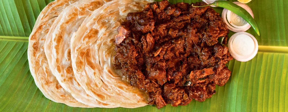 Layered porotta and Kerala beef fry on a banana leaf